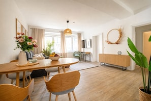 Un coin repas avec une table en bois, des chaises, un saladier de fruits et un vase de fleurs.