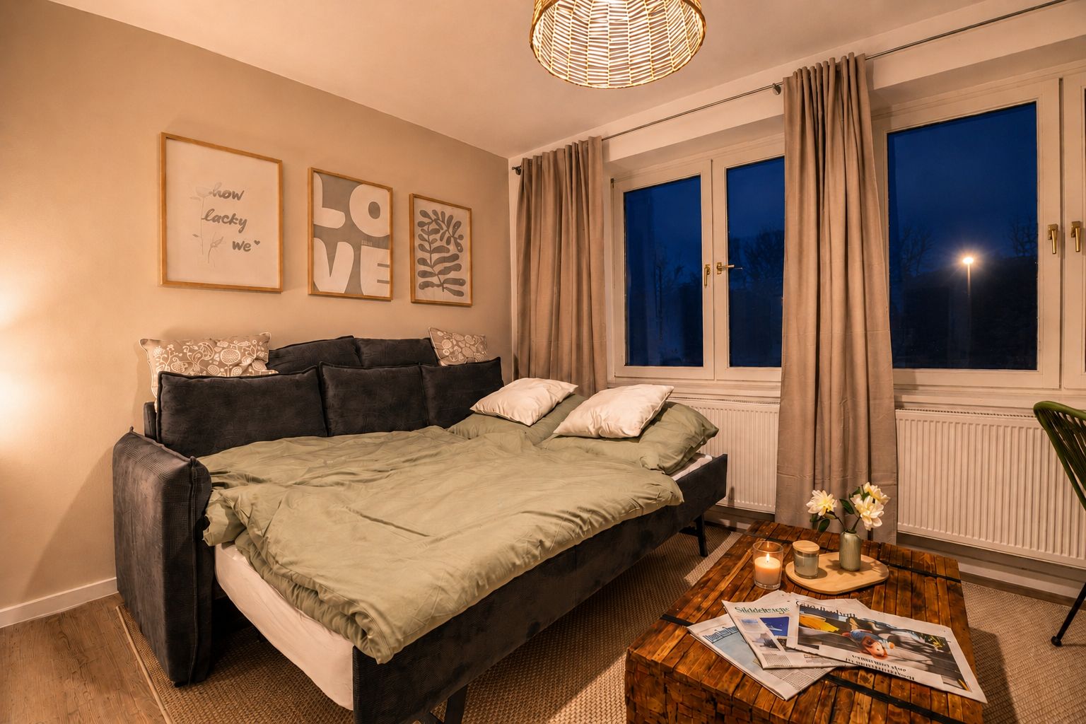 Ein Schlafzimmer mit einem Bett, einem Nachttisch mit Kerzen und einem Fenster mit Vorhängen.