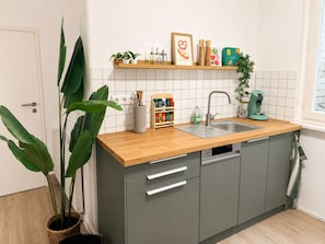 Une cuisine avec un plan de travail en bois, un évier et un four encastré. On y trouve également des plantes, un porte-épices et une machine à café sur le plan de travail.