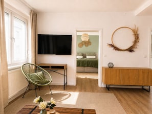A modern living room with a flat-screen TV, a green chair, a wooden cabinet, and a decorative wreath on the wall.