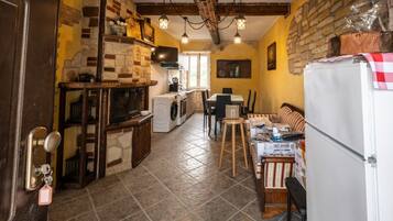 Cuina amb paret de pedra, bigues de fusta, rentadora i zona de menjador amb taula i cadires.