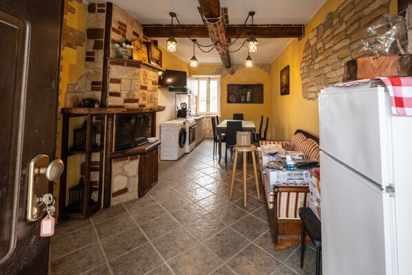 Een keuken met een stenen muur, houten balken, een wasmachine en een eethoek met een tafel en stoelen.