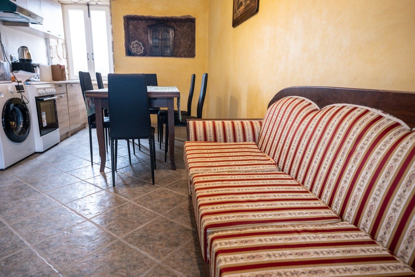 Ein gemütlicher, kompakter Wohnraum mit einer Couch, Esstisch, Stühlen und einer Waschmaschine.