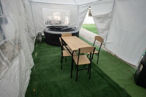 Une tente équipée d’une table et de chaises, d’un jacuzzi et d’un revêtement de sol en gazon synthétique.