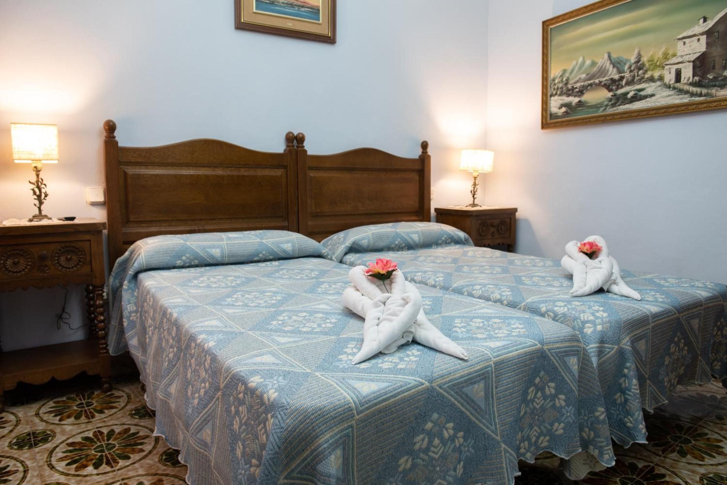 Une chambre d'hôtel avec une tête de lit en bois, deux lits avec une literie à motifs bleus et deux lampes de chevet.