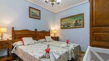 A hotel room with a wooden bed, two bedside tables, a chandelier, and two paintings on the walls.