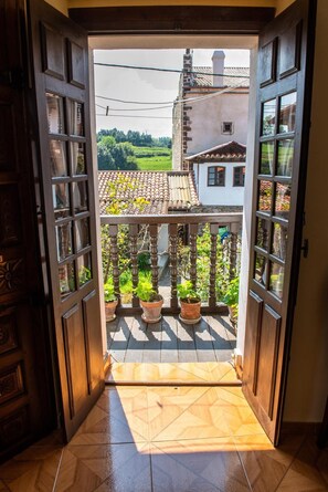Eine offene Holztür, die auf einen Balkon mit Fliesenboden und Pflanzgefäßen führt.