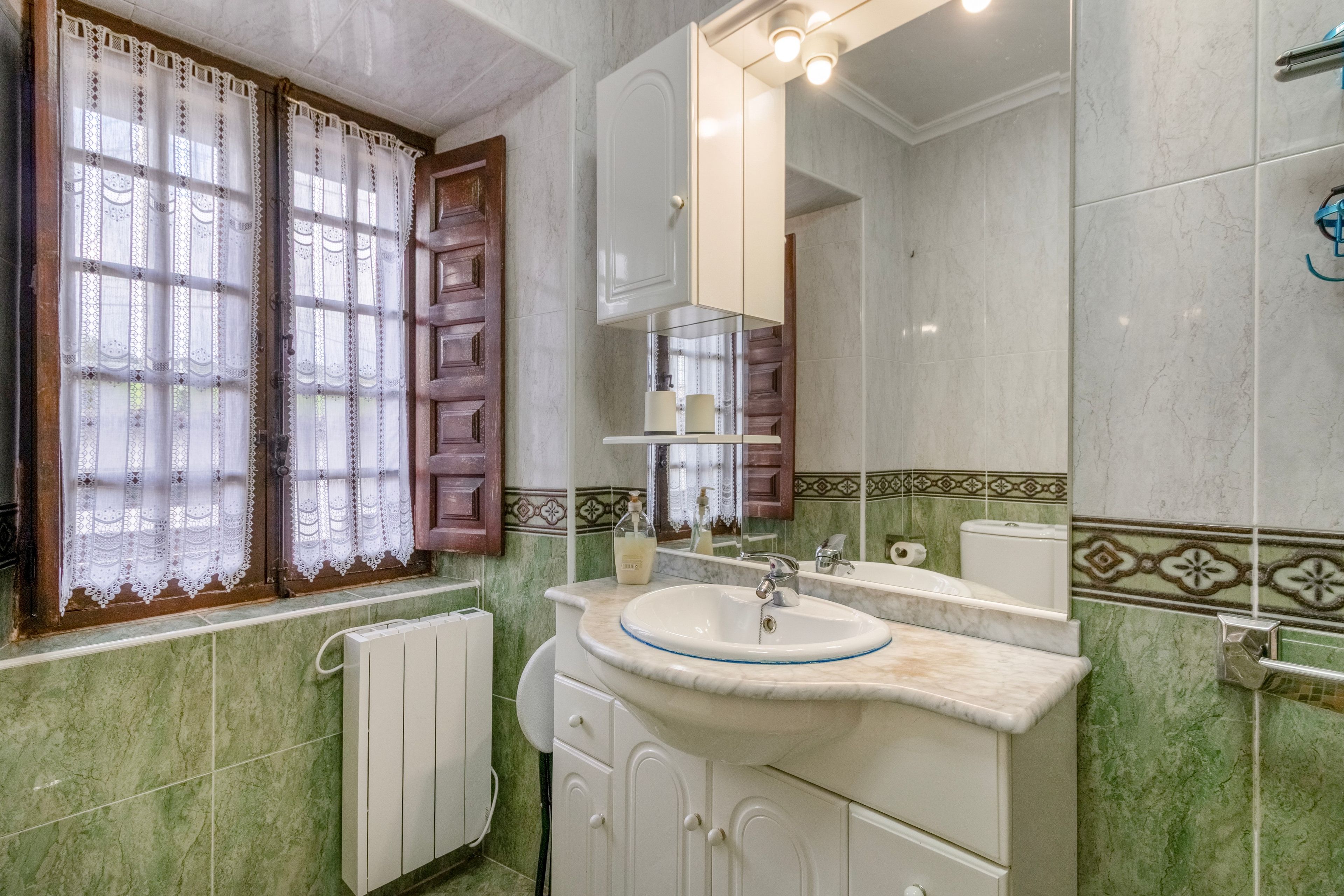 Un baño con lavamanos, espejo y ventana con cortinas de encaje.