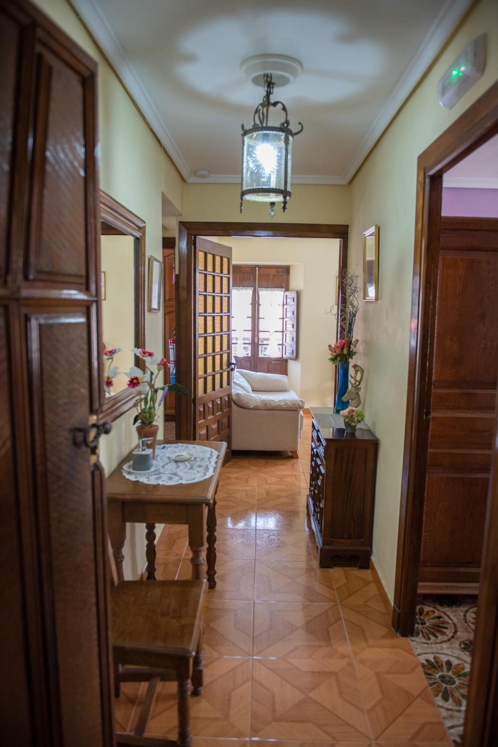 Un couloir avec une porte en bois, une table recouverte d’une nappe en dentelle, une chaise, un canapé et une lampe décorative.