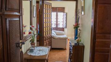 Un couloir avec une porte en bois, une table recouverte d’une nappe en dentelle, une chaise, un canapé et une lampe décorative.