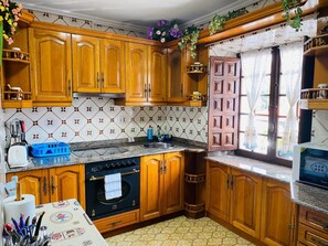 Eine Küche mit Holzschränken, einem Herd, einer Spüle und einem Fenster mit Vorhängen.