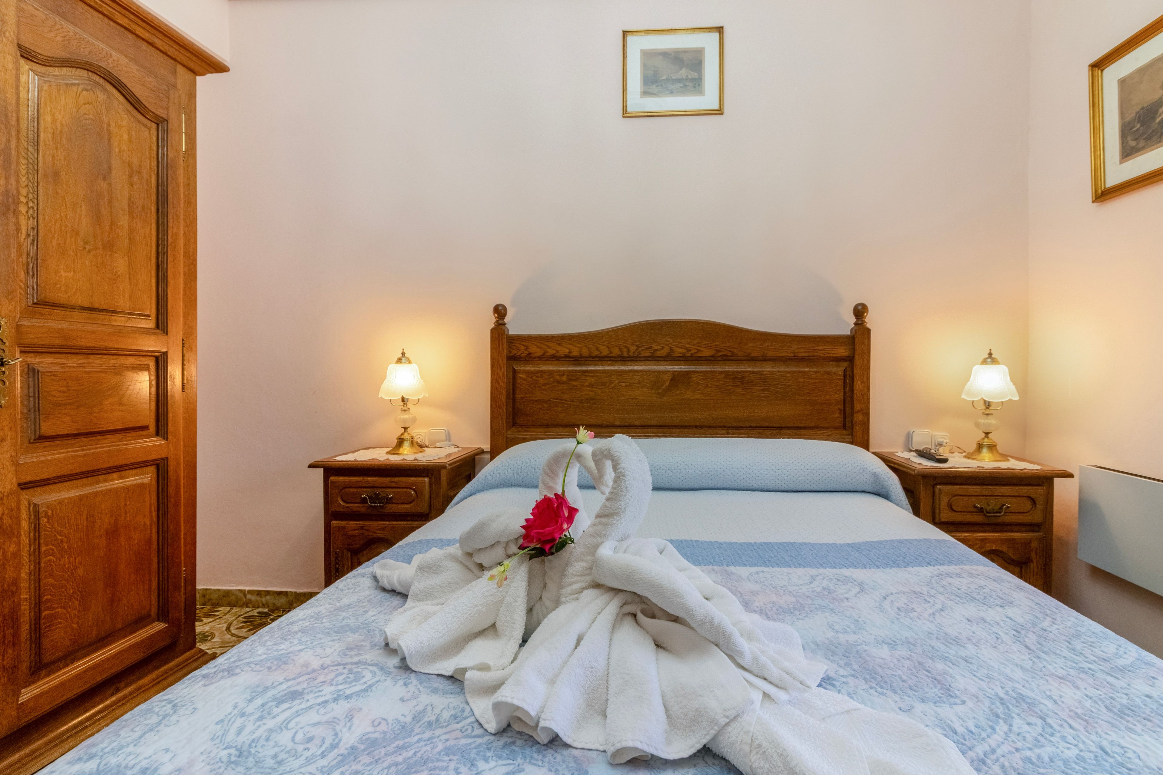 Habitación de hotel con un armario de madera, una cama con colcha azul y blanca a rayas, dos lámparas de noche y un cuadro en la pared.