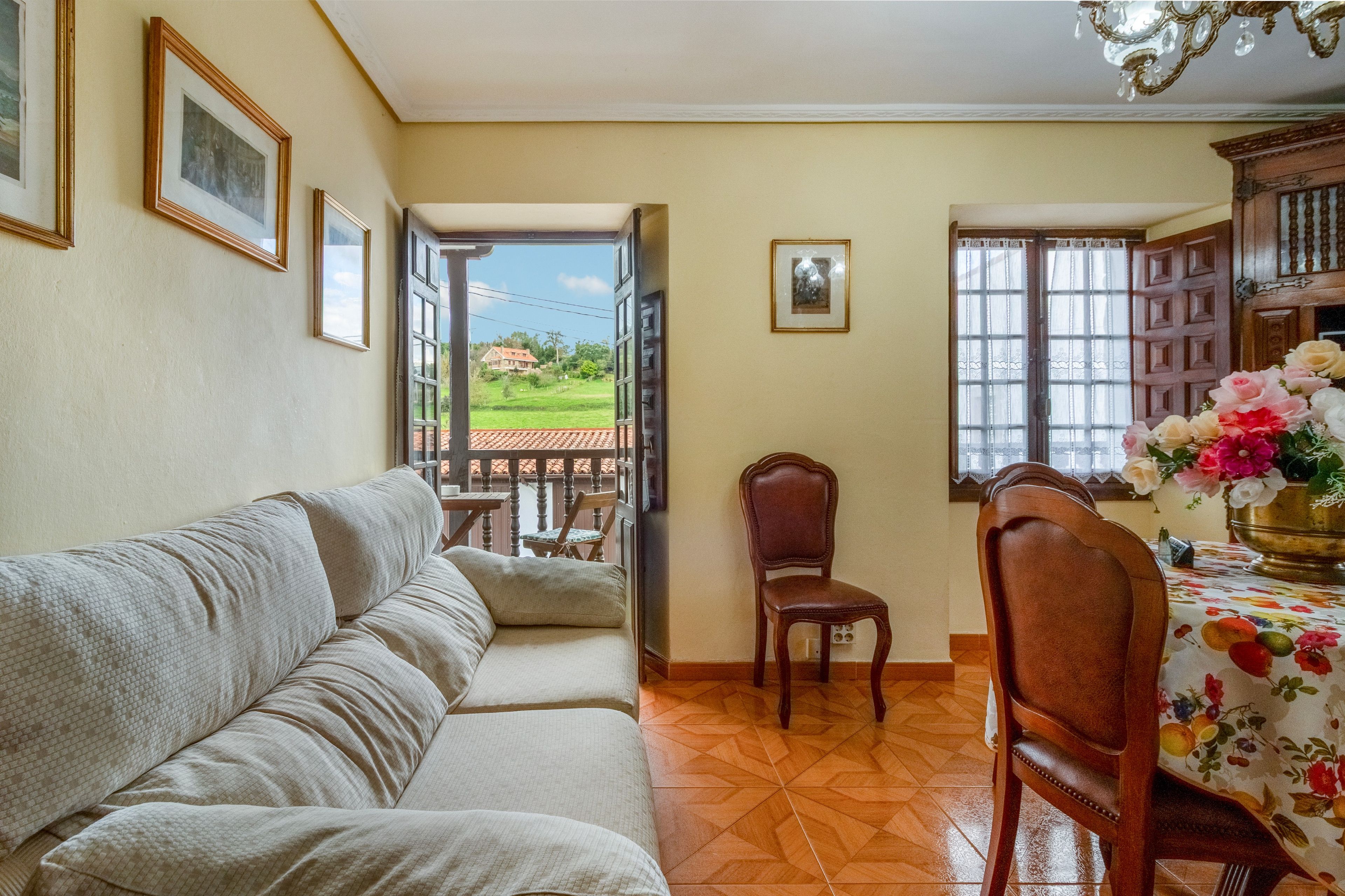 Ein Wohnzimmer mit einer Couch, einem Esstisch mit Stühlen und Blick auf ein Haus durch eine offene Tür.