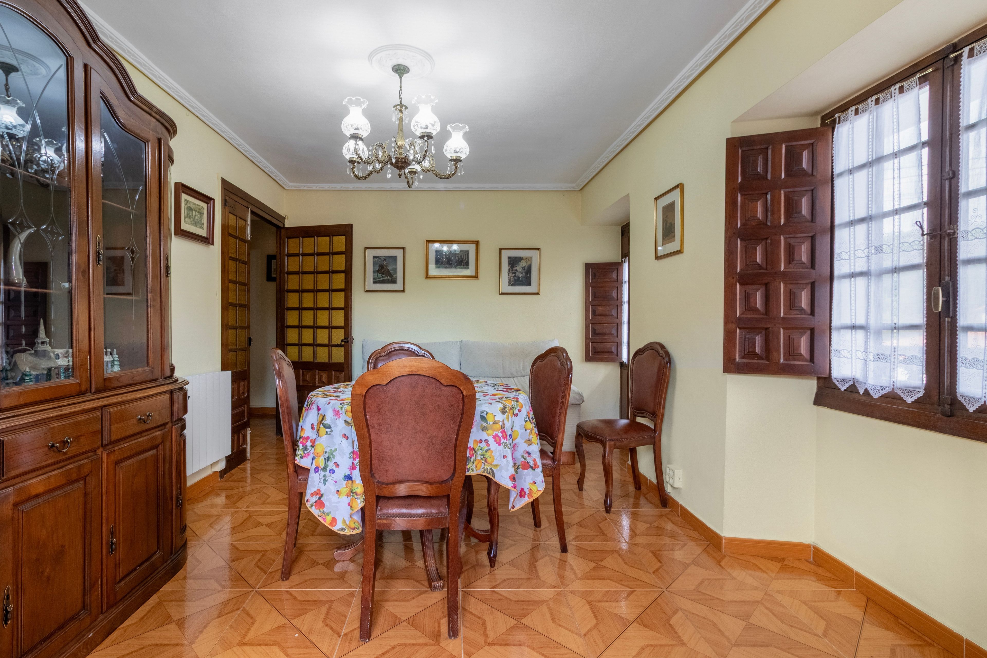 Un coin repas avec une table et des chaises en bois, un lustre et un buffet aux portes vitrées.