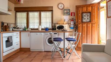Cocina compacta con lavadora, microondas y lavaplatos. Hay dos taburetes de bar y un sofá blanco.