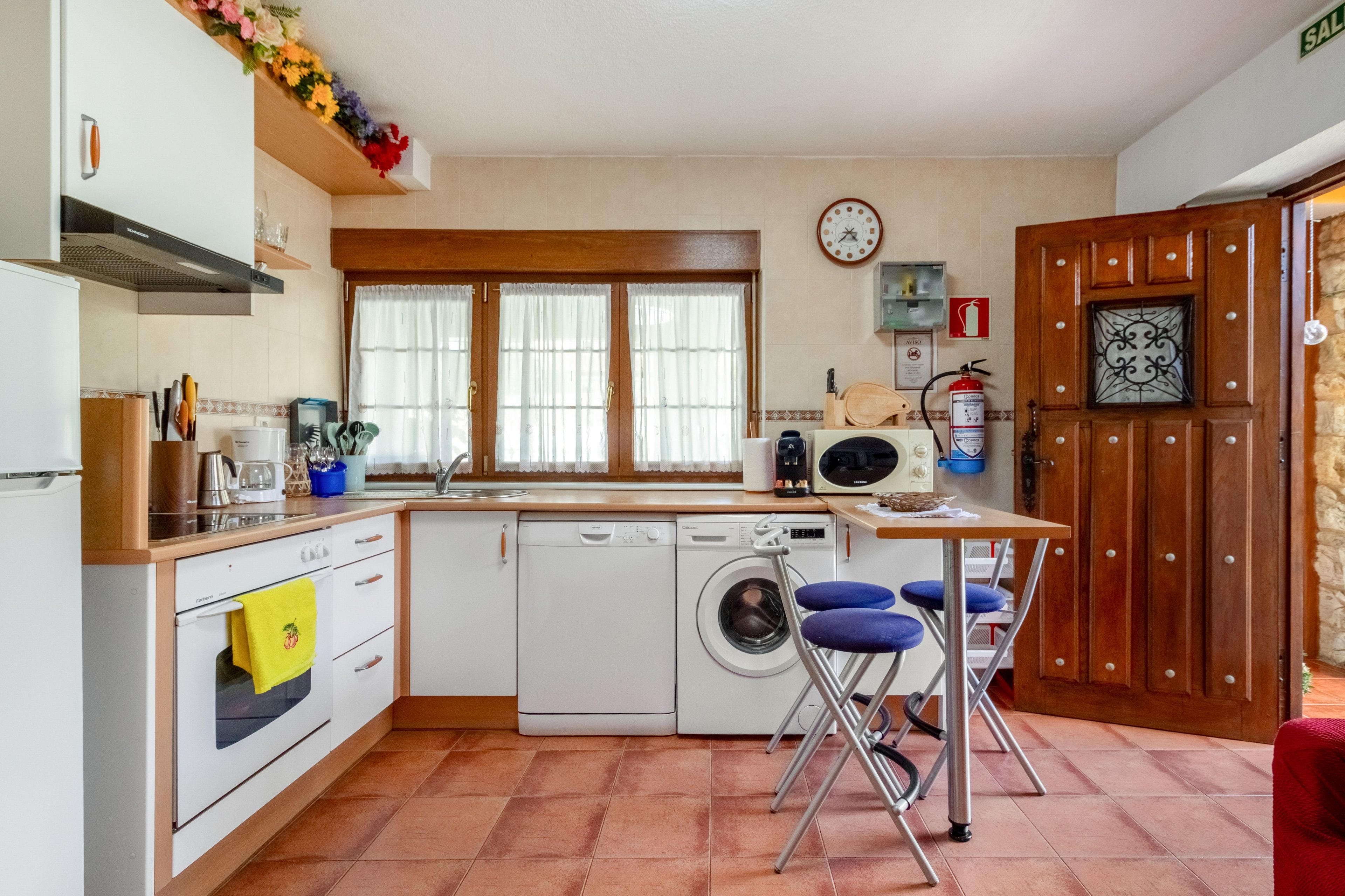 A compact kitchen with a washing machine, a coffee maker, and a clock on the wall.