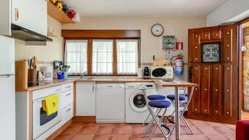 A compact kitchen with a washing machine, a coffee maker, and a clock on the wall.