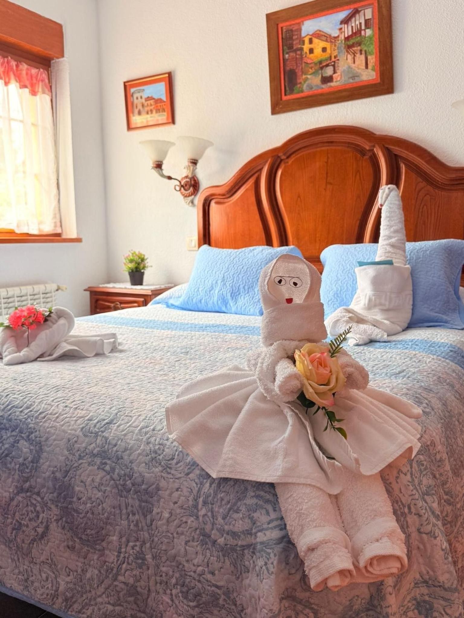 A hotel room with a wooden headboard, a bed with blue and white bedding, and two towels shaped like a person holding a rose.