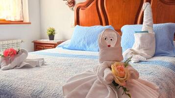 A hotel room with a wooden headboard, a bed with blue and white bedding, and two towels shaped like a person holding a rose.