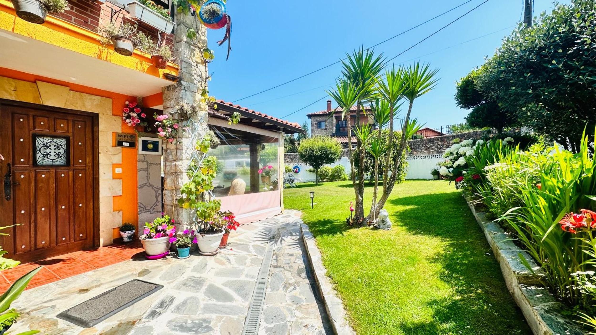 A residential property with a stone entrance, a wooden door with a decorative glass panel, and a small garden with various plants and a lawn.