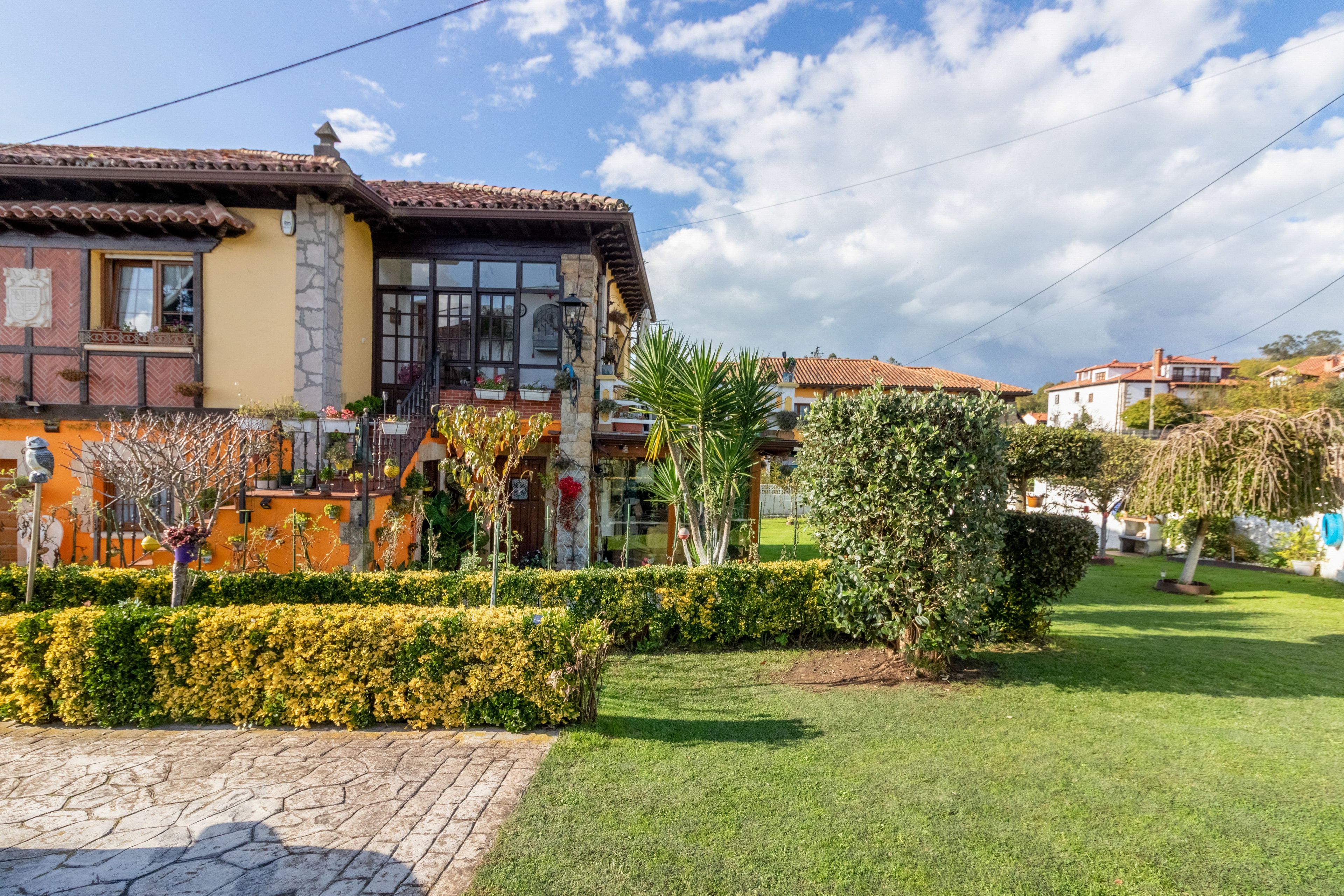 Un edificio tradizionale con tetto in tegole, facciata in pietra e un giardino curato con siepi e prato.