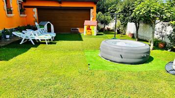 A backyard with a hot tub, lawn chairs, and a small playhouse.