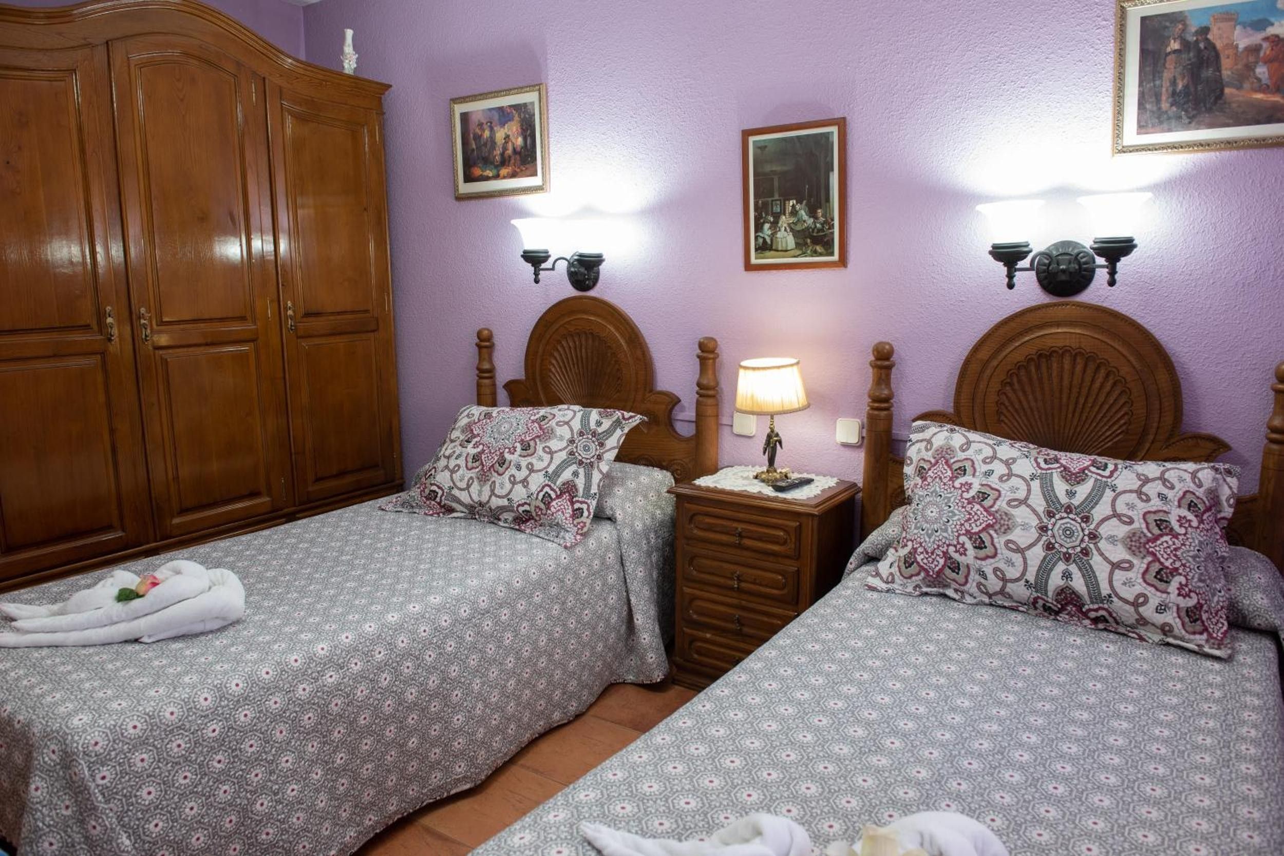 Un dormitorio con dos camas, cabeceros de madera, un armario y lámparas de pared.