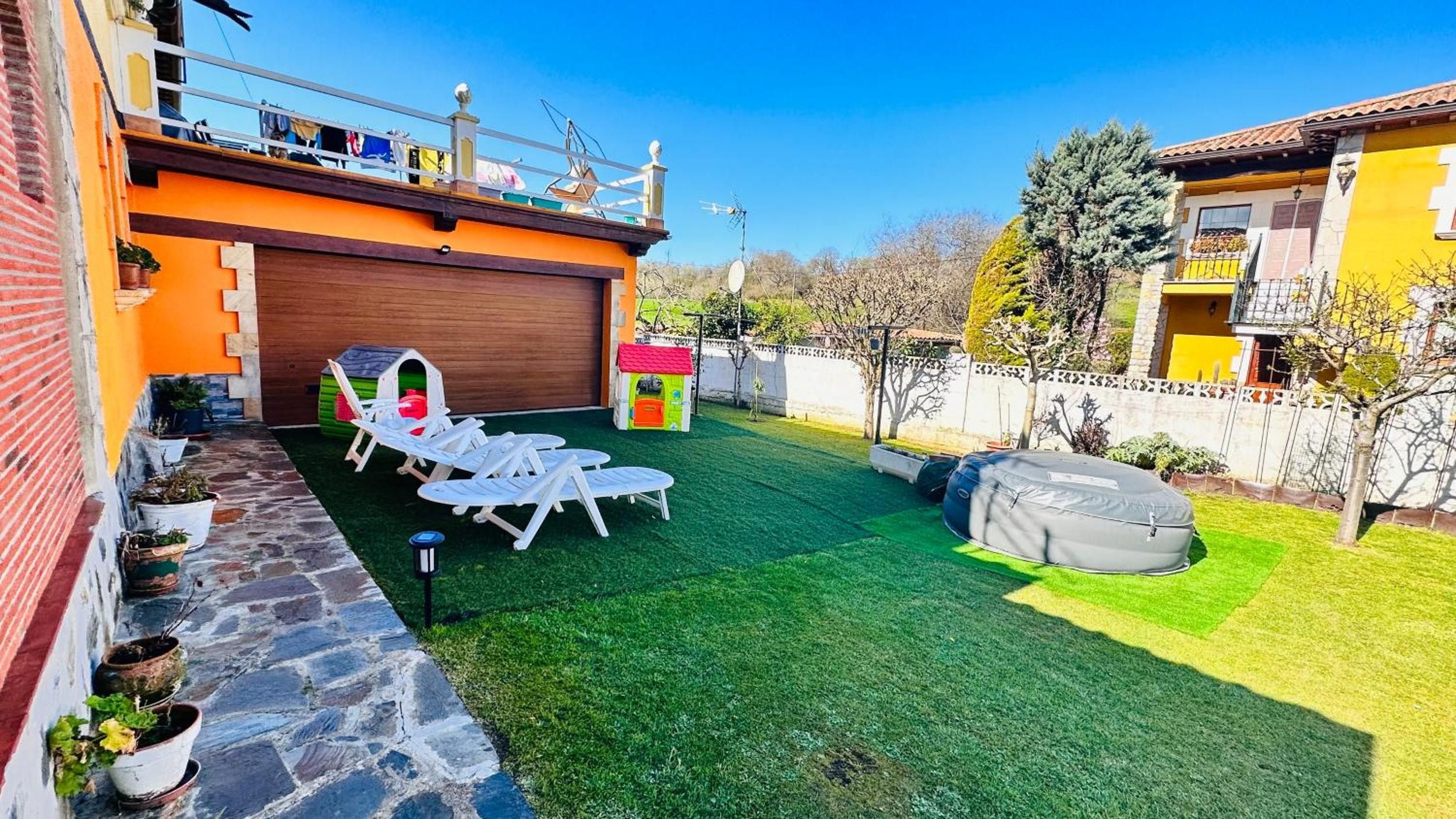 A residential backyard with artificial grass, a playhouse, a barbecue area, and a covered seating area.