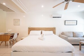 Ein Hotelzimmer mit einem großen Bett, einem Holzkopfteil, einem Esstisch mit Stühlen, einer Couch und einem Deckenventilator.