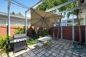 En terrasse med grill, bord og parasol.