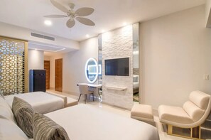 Een moderne hotelkamer met twee bedden, een bureau met stoel, een televisie bevestigd aan een stenen muur en een plafondventilator.