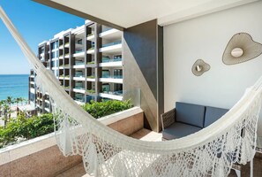 Ein Balkon mit einer weißen Hängematte, einer Sitzecke und Blick auf ein modernes Gebäude mit Balkonen, das zum Meer hinabragt.