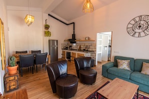 A modern living room with a sofa, chairs, and a coffee table. There is a kitchen area with a refrigerator, oven, and sink. - Farm Lodges Olive, Casa Alfarrobeira, Moncarapacho Countryside (moncarapacho)