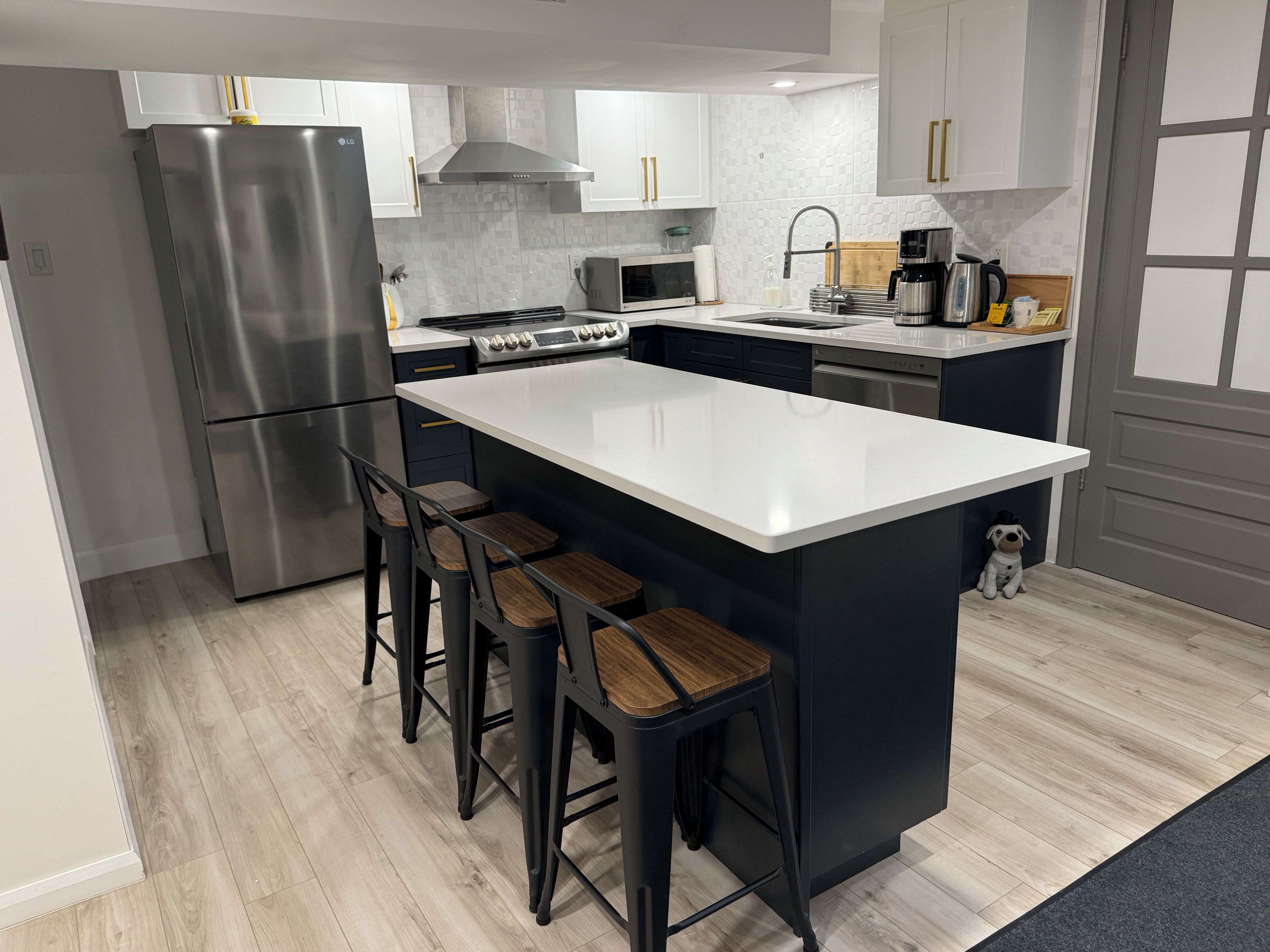 A modern kitchen with a stainless steel refrigerator, a built-in stove, a microwave, and a sink with a faucet. There are three stools at the island.