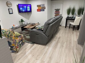A living room with a grey sofa, a colorful armchair, a wooden coffee table, and a flat-screen TV mounted on the wall. - Aura Basement Unit 2 / Self-Check-In, Wi-Fi, and 1 Free Parking Space / Niagara Falls, ON (Niagara Falls)
