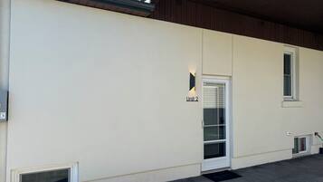 Eine Gebäudefassade mit einem 'Unit 2' Schild, einer Tür mit Fenster und einem kleinen Lüftungsgitter.