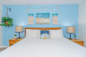 A bedroom with a bed, two nightstands, a headboard, wall art, and a hanging plant. - Ocean Views & Coastal Comfort at Meridian Plaza 508 (Myrtle Beach)