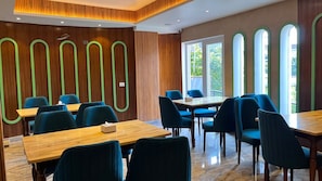 Ein Konferenzraum mit Holztischen und blauen Stühlen, großen Fenstern und einer Holzwand mit grünen Akzenten.