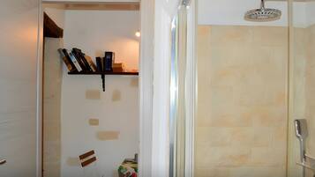 Une salle de bain avec une douche, une chaise et une étagère contenant des livres et une boîte.