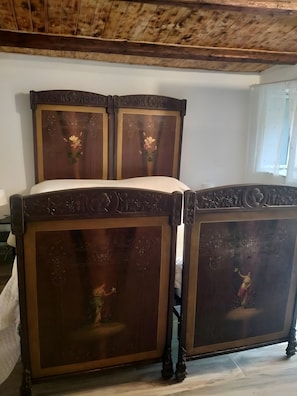 Ein hölzernes Bett mit aufwendigen Schnitzereien und einer weißen Matratze in einem Zimmer mit Holzboden und weißen Wänden.