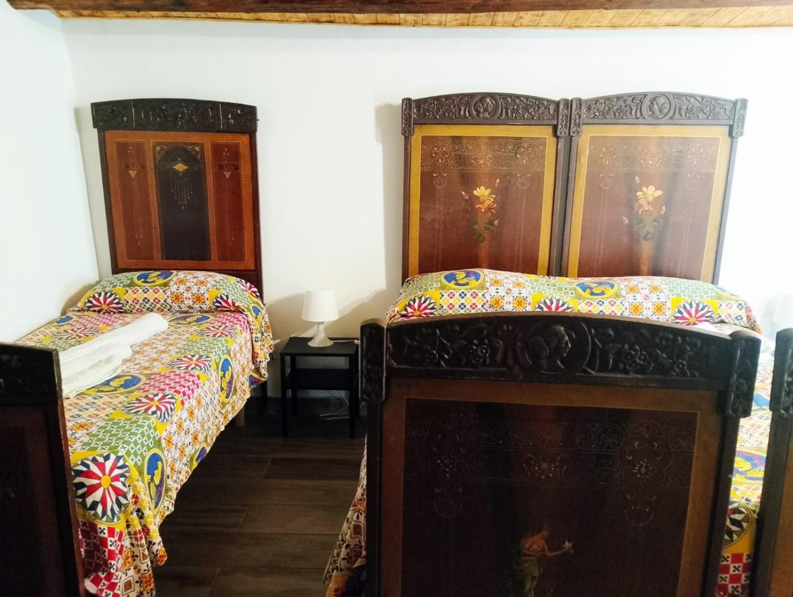 Une chambre avec deux lits en bois dotés de têtes de lit décorées, une petite table de chevet avec une lampe et une couverture de lit colorée à motifs.
