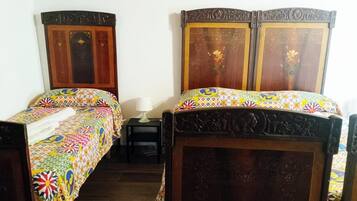 Une chambre avec deux lits en bois dotés de têtes de lit décorées, une petite table de chevet avec une lampe et une couverture de lit colorée à motifs.