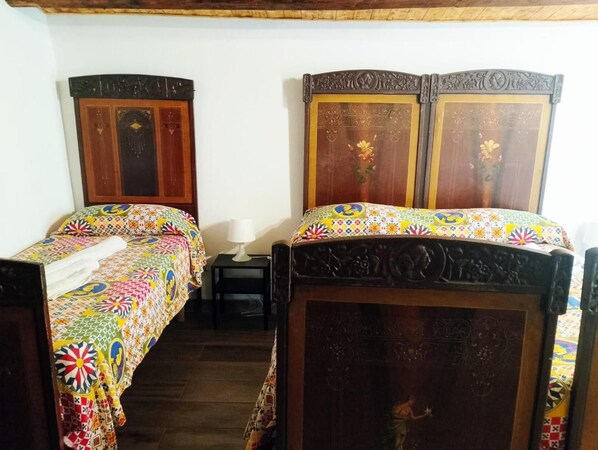 Habitació amb dos llits de fusta que tenen els capçals decorats, una petita taula de nit amb una làmpada, i un edredó estampat i colorit.