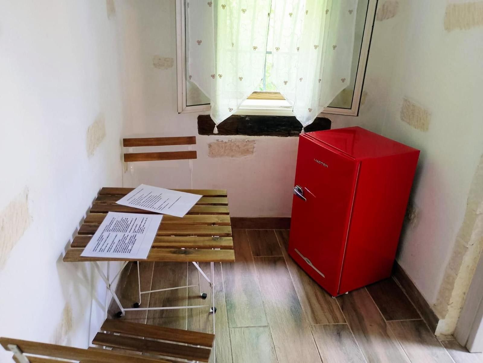 Une petite pièce avec un banc en bois, un meuble rouge et une fenêtre ornée d’un rideau à motifs floraux.