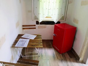 Habitació petita amb una banca de fusta, un armari vermell i una finestra amb cortina floral.