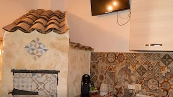 Una cocina con salpicadero de azulejos, cafetera, televisor montado en la pared y mueble moderno.