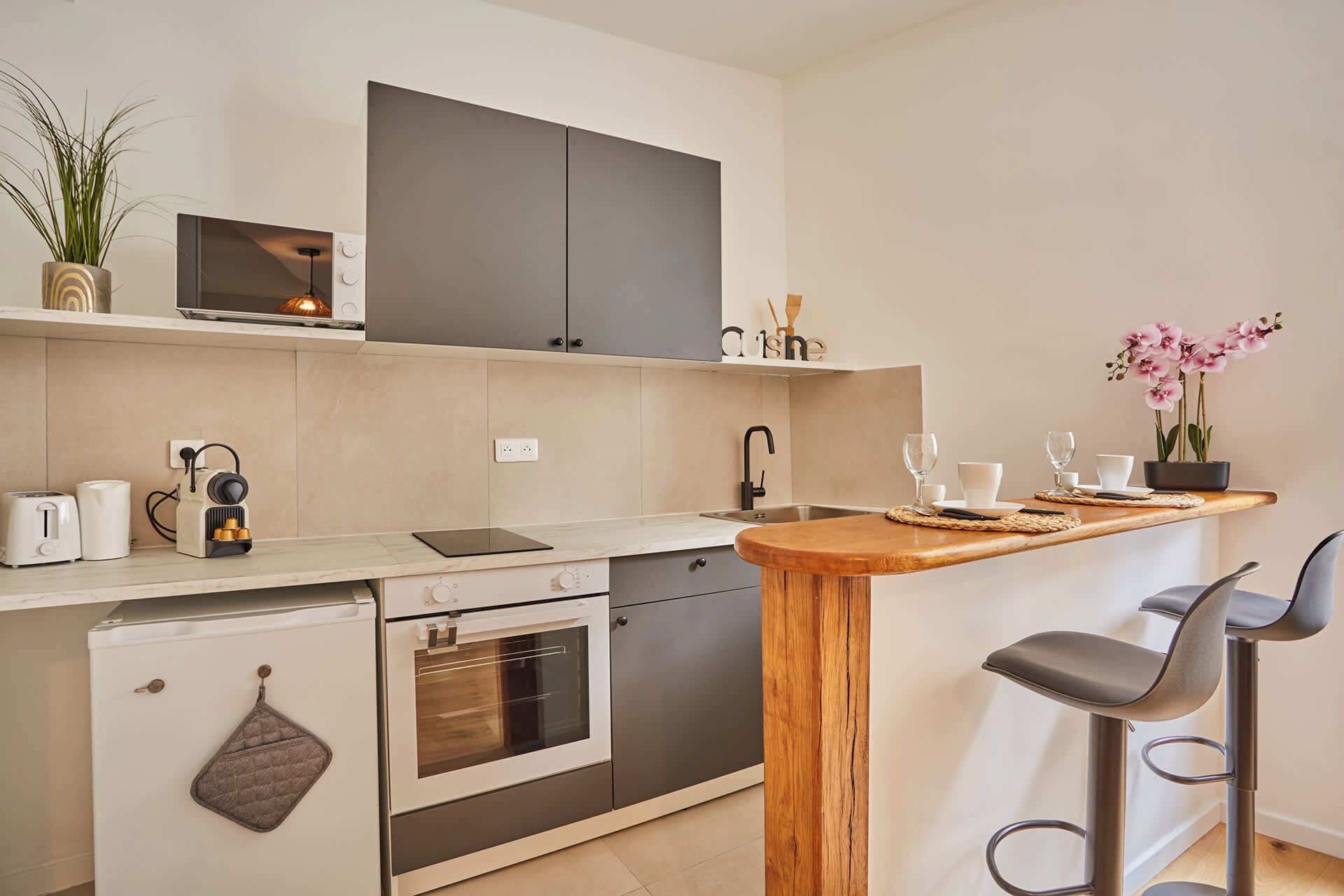 Eine moderne Küche mit Einbauofen, kleinem Kühlschrank, Kaffeemaschine und einer Bar mit Sitzgelegenheiten.