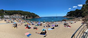 A crowded beach with people sunbathing and swimming, surrounded by buildings and boats on the water. - Comfortable, authentic, and just steps from Tamariu Beach—Apartment sleeps 6 (Tamariu)