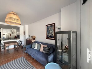 A modern living room with a sofa, a dining area, and a kitchen in the background. - Comfortable, authentic, and just steps from Tamariu Beach—Apartment sleeps 6 (Tamariu)