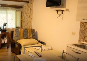 Ein Hotelzimmer mit Bett, einem an der Wand befestigten Fernseher, einem kleinen Tisch und einer Küchenzeile.